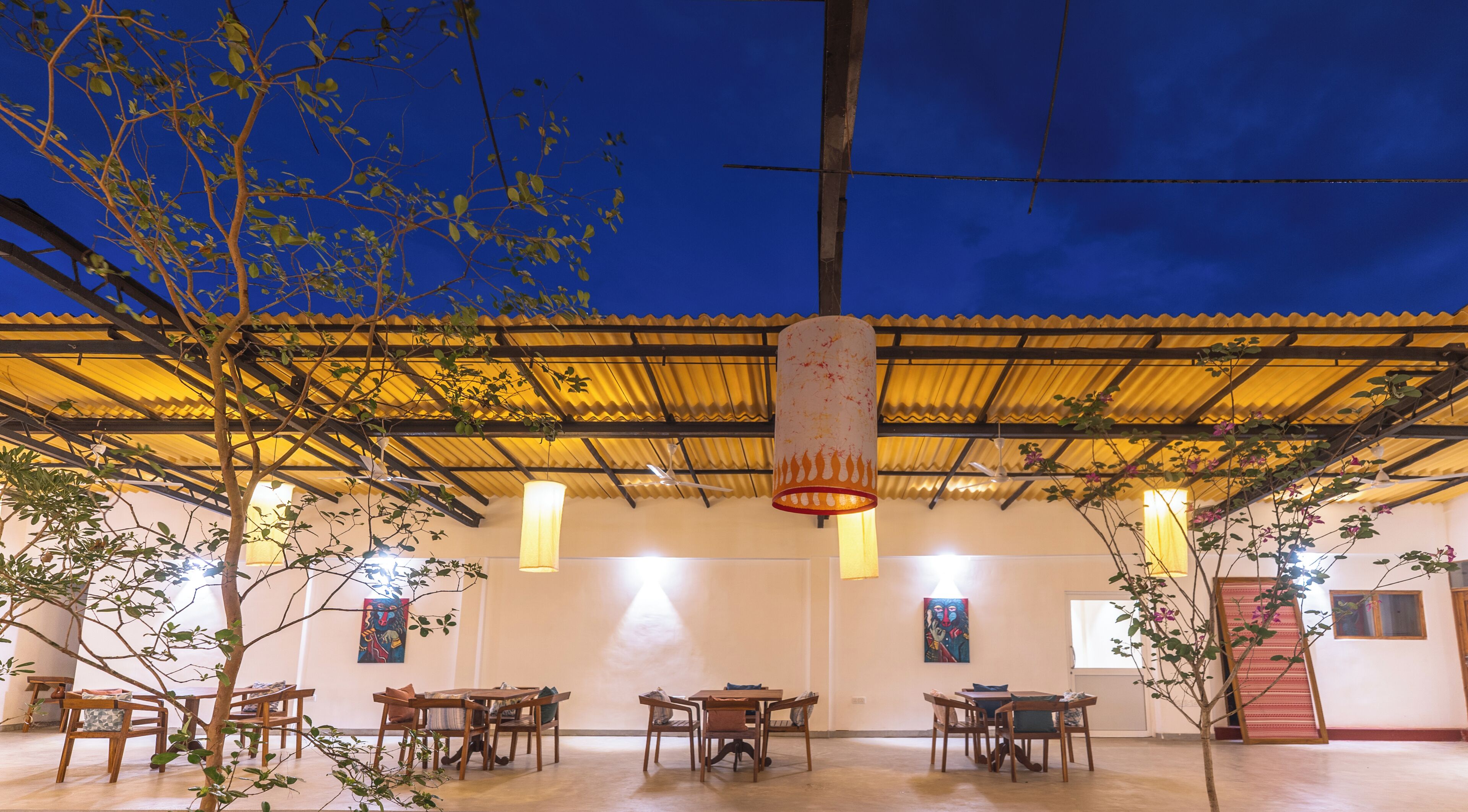 An outdoor dining area with tables and chairs, a pergola with yellow roofing, and hanging lamps.