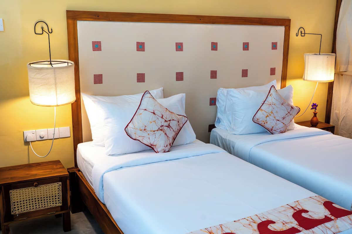 A hotel room with two beds, a wooden headboard, bedside lamps, and a nightstand with a lamp.