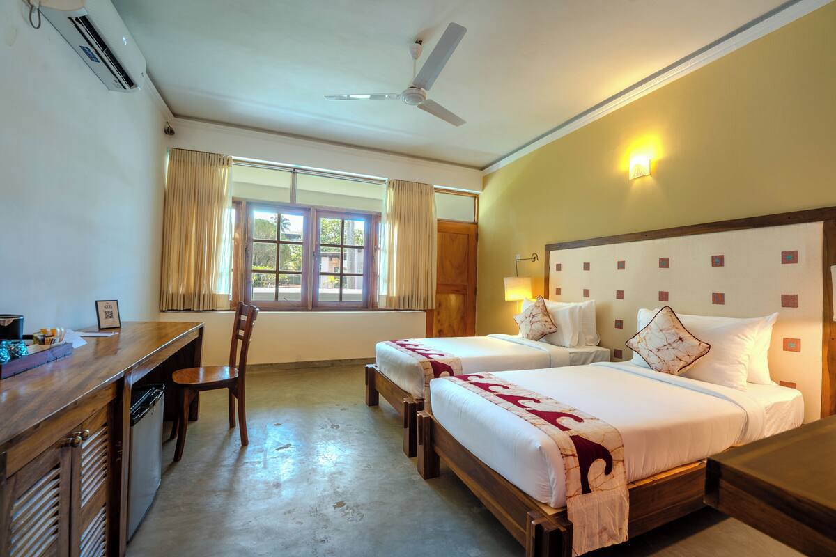 A hotel room with two beds, a desk, a chair, and a ceiling fan.