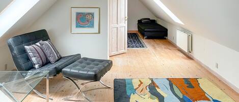 Un cuarto estilo loft con techo alto, un sillón de cuero negro, una mesa de vidrio, una alfombra colorida y un sofá negro.
