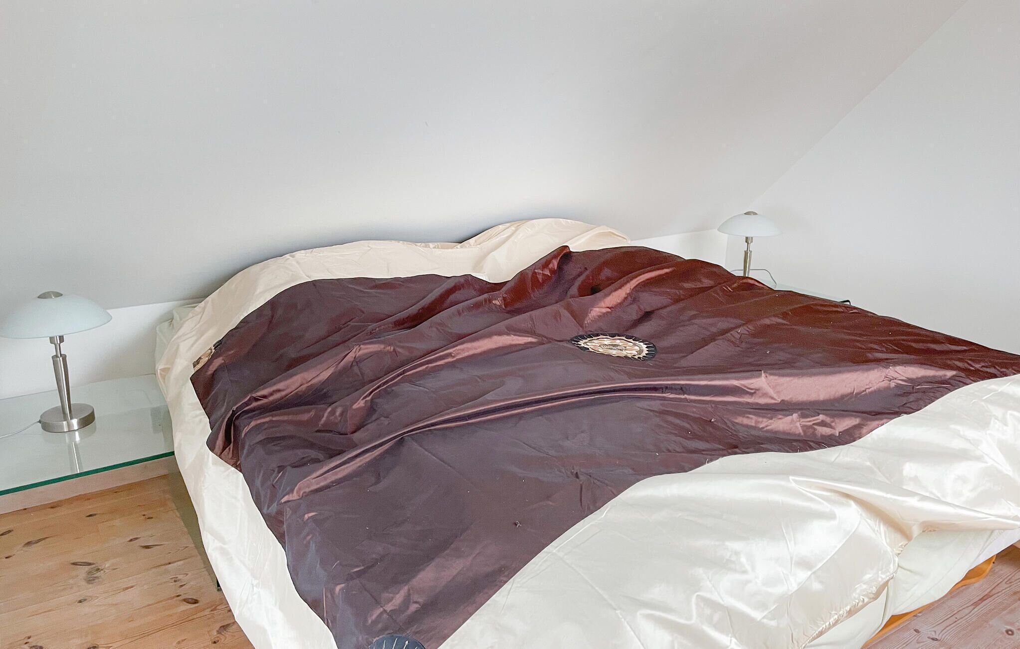Un lit recouvert d’une couverture blanche et marron, deux lampes de chevet et un plancher en bois.