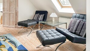 Ein Loft-Wohnzimmer mit Glastisch, Lederhockern und einer hohen Decke mit Oberlicht.