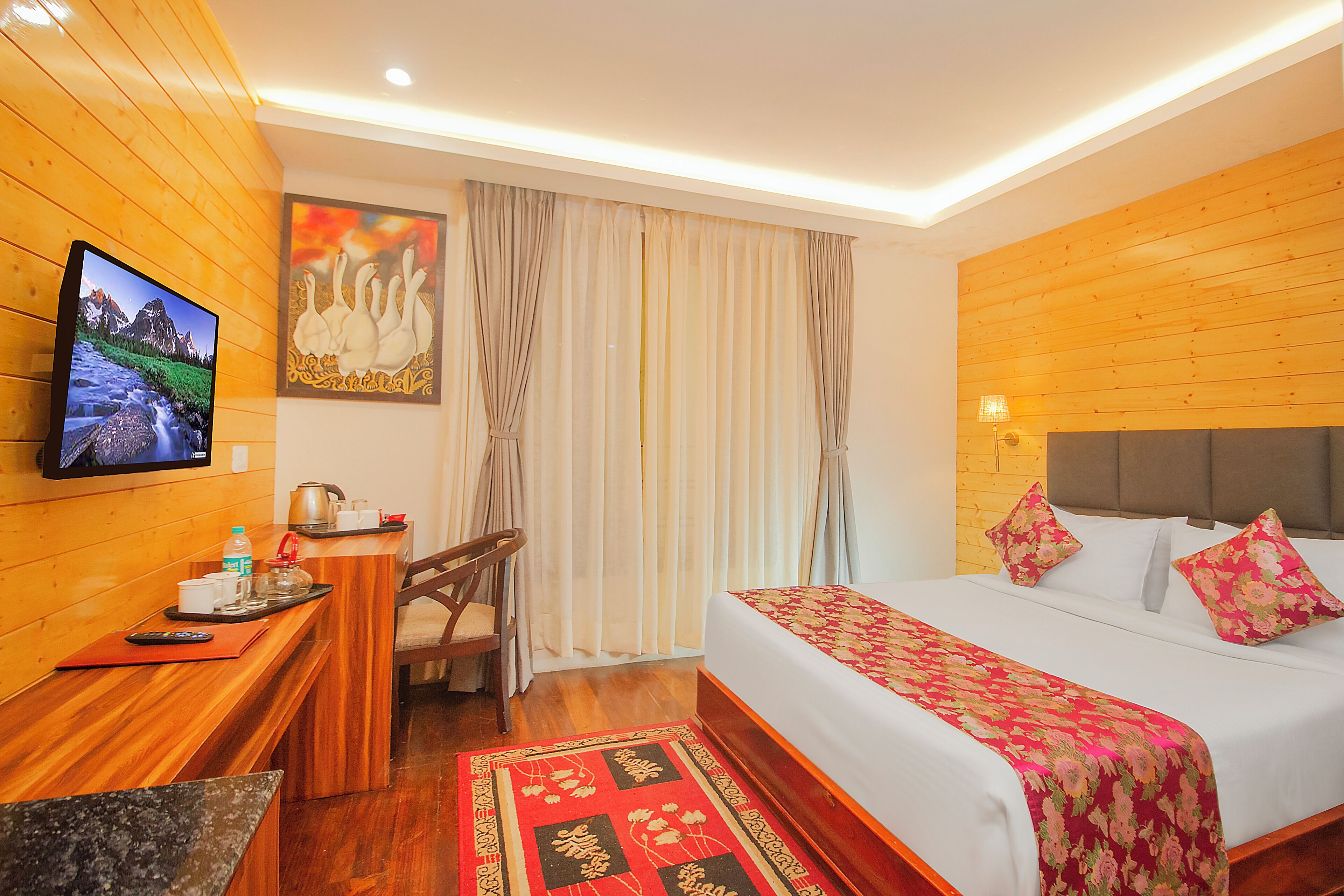 Habitación de hotel con pared de madera, cama con ropa de cama floral, escritorio con televisor y ventana con cortinas.