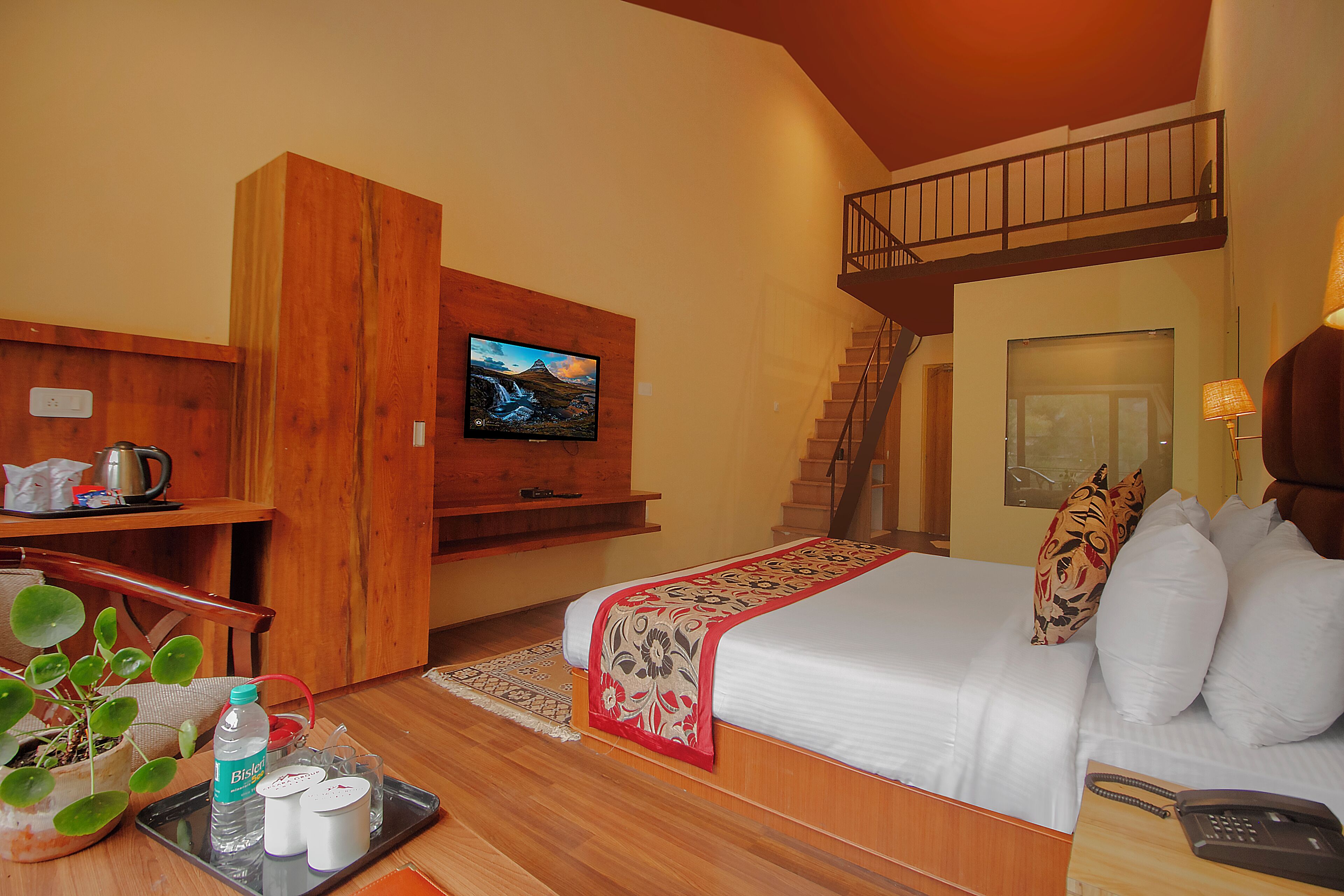 A hotel room with a bed, a TV, a desk with a kettle, a plant, and a tray with toiletries.