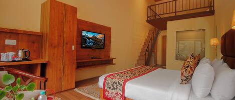 A hotel room with a bed, a TV, a desk with a kettle, a plant, and a tray with toiletries.