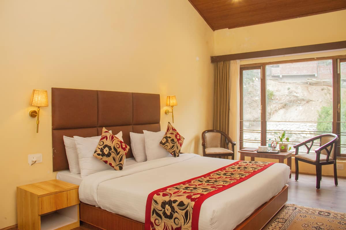 Habitación de hotel con una cama grande, dos lámparas de noche, una silla, una mesita y vistas al exterior.