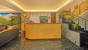 Zona de recepción con mostrador de madera, un sofá y una escalera adornada con plantas en macetas.