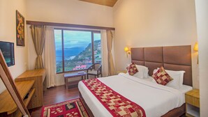 Un dormitorio con una cama grande, un escritorio, una silla, una ventana con cortinas y vistas a un paisaje montañoso.