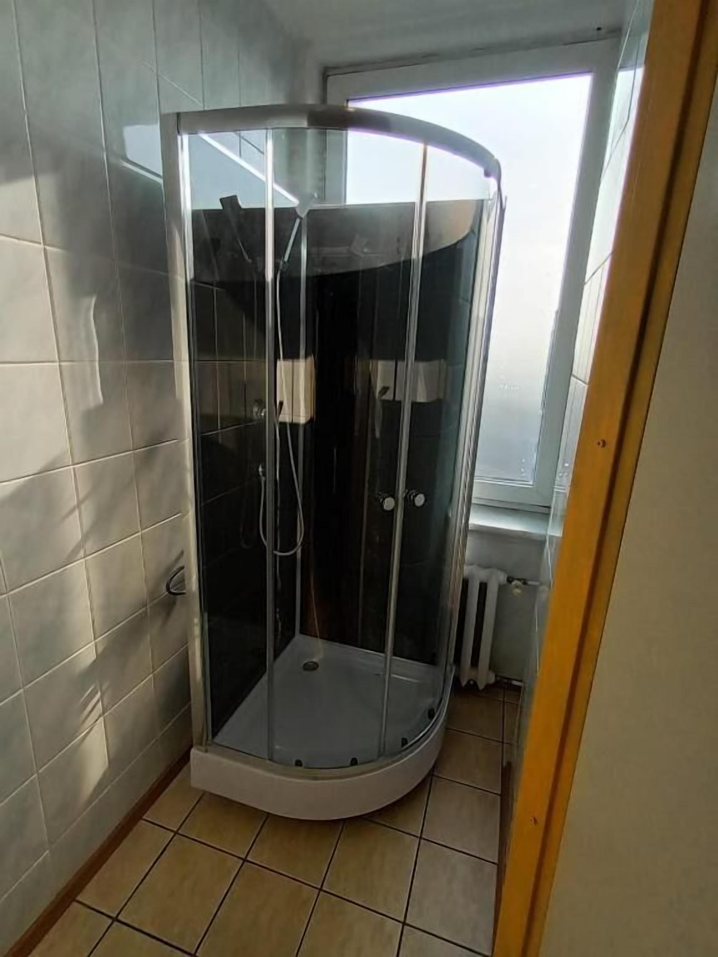 Een douchehoek met een glazen wand, betegelde muren en een raam.