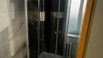 A corner shower with a glass enclosure, tiled walls, and a window.