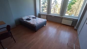 A bedroom with a bed, a chair, and large windows with a view of trees.