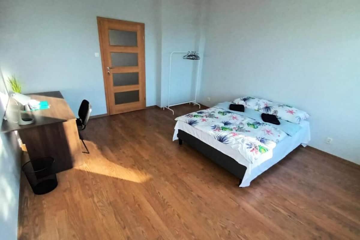 Ein Schlafzimmer mit Holzboden, einem Bett mit floralem Bettzeug, einem Schreibtisch mit Stuhl und einer Tür.
