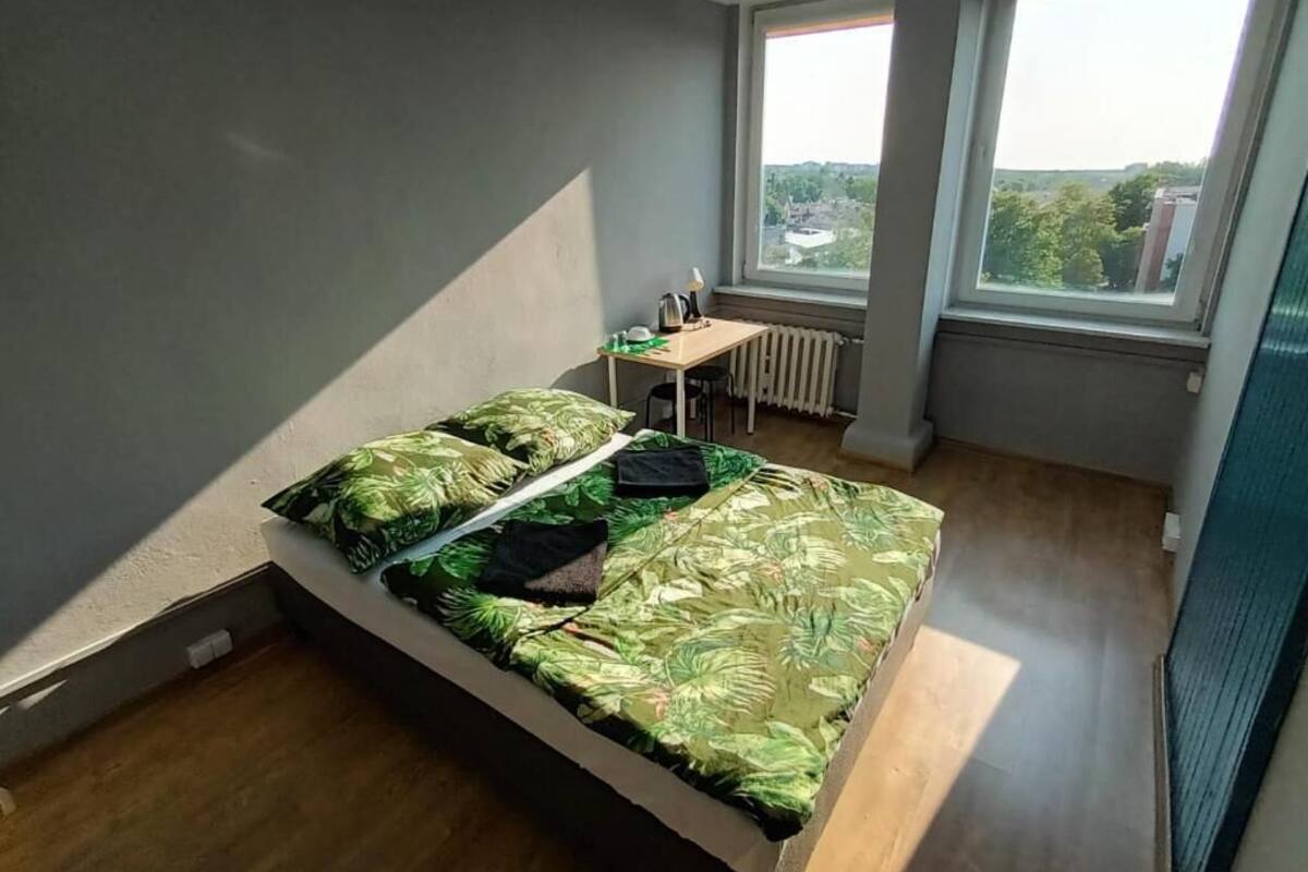 Ein Schlafzimmer mit Bett, Schreibtisch und Blick auf die Stadt durch große Fenster.