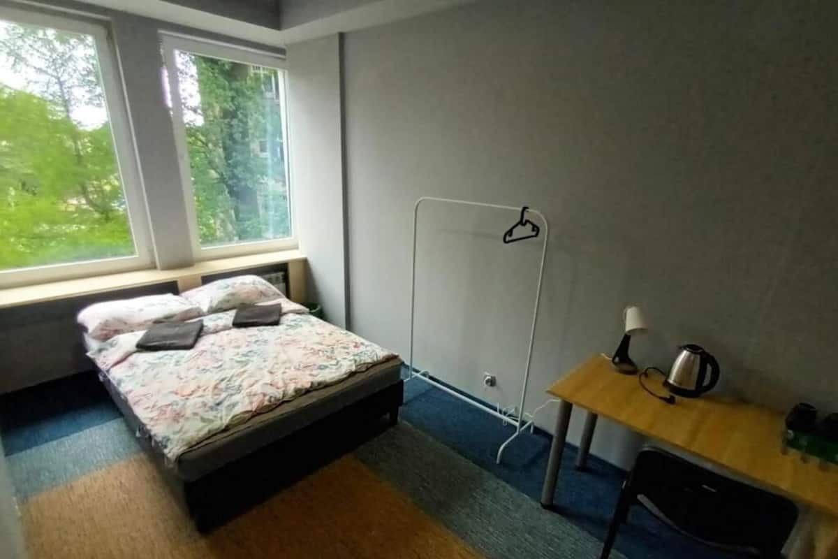 Ein Schlafzimmer mit einem Bett, einem Holztisch mit Wasserkocher und einem Fenster mit Blick auf Bäume.