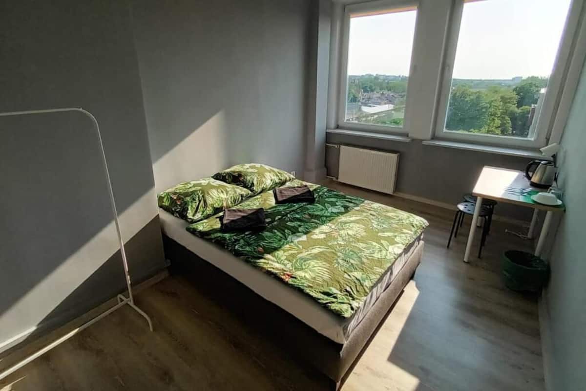 Ein kleines Schlafzimmer mit einem Bett, einem Schreibtisch und einem Fenster mit Blick auf eine Stadtlandschaft.