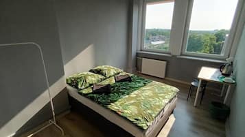 A small bedroom with a bed, a desk, and a window overlooking a cityscape.