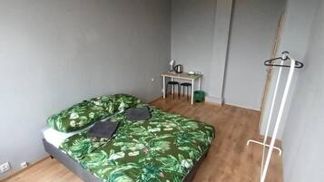 A bedroom with a bed, a desk, and a hanging clothes rack.