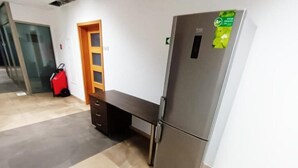 Una habitación de hotel con un refrigerador, una puerta de madera y una maleta roja.