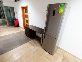 Una habitación de hotel con un refrigerador, una puerta de madera y una maleta roja.