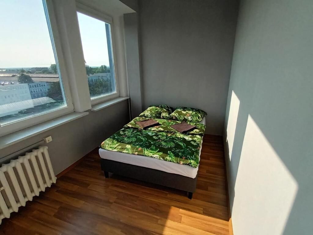 Un dormitorio pequeño con cama, un radiador y una ventana con vistas a edificios.