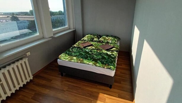 A small bedroom with a bed, a radiator, and a window with a view of buildings. - Fantastic Inn Zielona Góra - Sulechowska (Zielona Góra)