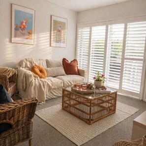 A cozy living room with a sofa, a wicker coffee table, and a window with blinds. - The Oaks Resort - Sea Salt One Bedroom (Salamander Bay)