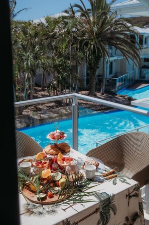 A balcony with a table set for breakfast overlooking a swimming pool and palm trees. - The Oaks Resort - Sea Salt One Bedroom (Salamander Bay)