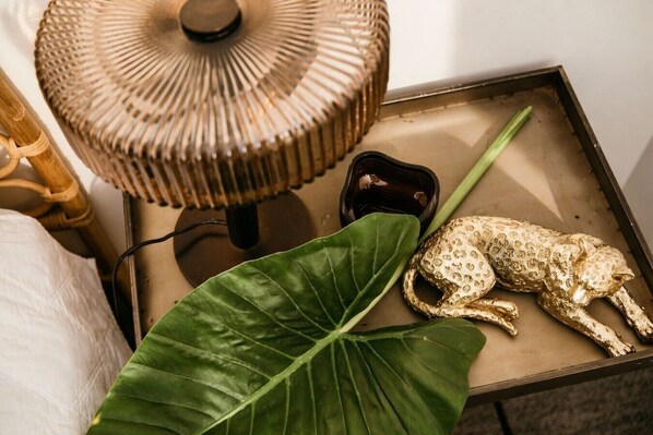 A room with a large green leaf, a golden animal figurine, a small black object, and a woven lamp.