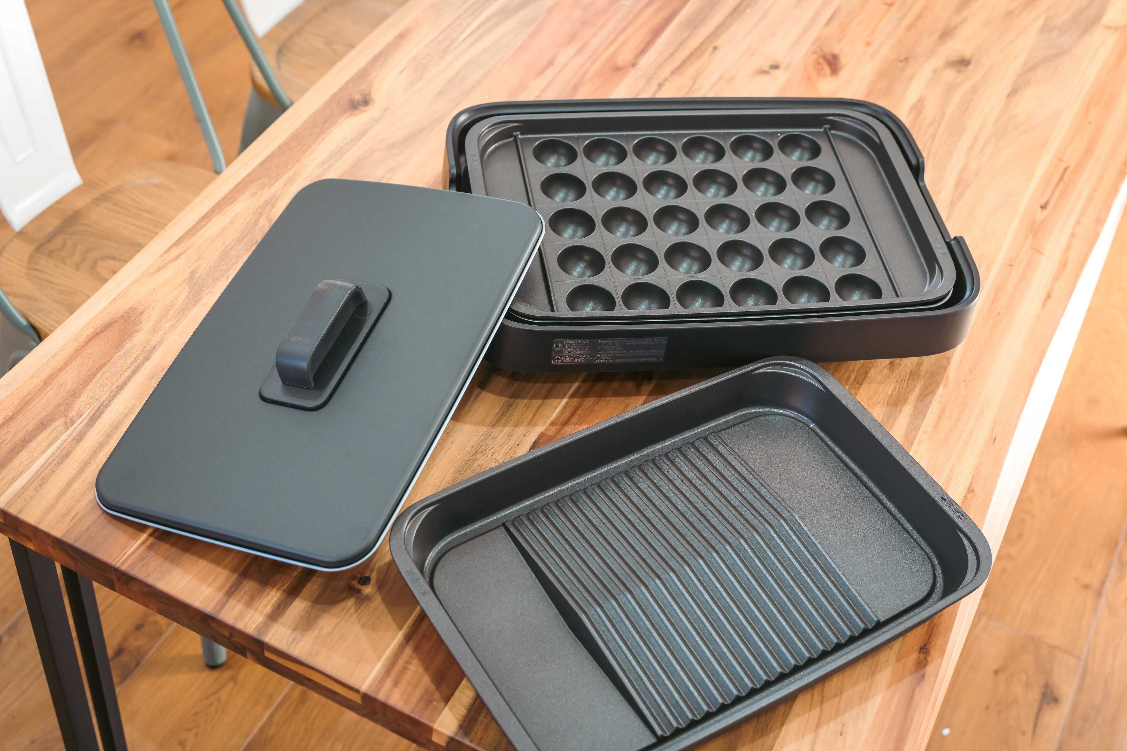 A table with a black tray with a handle, a black tray with circular indentations, and a black tray with ridges.
