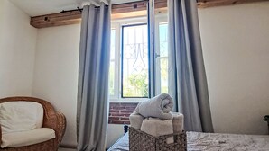A bedroom with a bed, a wicker chair, a window with curtains, and a view of greenery outside. - Stilvolles Landhaus an der Algarve by Interhome (Algoz)