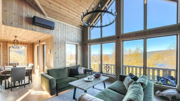 A spacious living area with a large window, a dining table, and a sofa. - Amazing home in Røn with sauna (Røn)