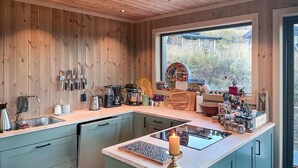 A modern kitchen with wooden walls, a large window, and various cooking appliances. - Amazing home in Røn with sauna (Røn)