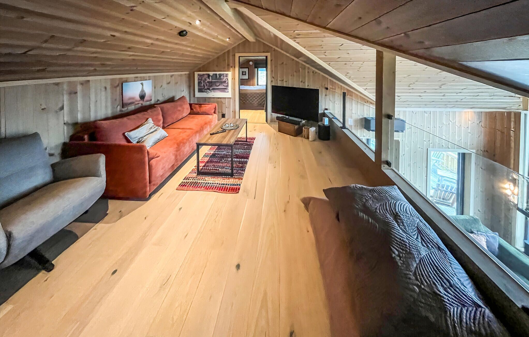 Amplio espacio tipo loft con techo alto, vigas de madera, un ventanal, un sofá, un televisor y una alfombra.