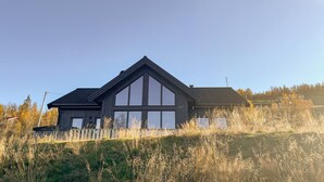 A modern house with a large central window, a sloped roof, and a wooden fence in front. - Amazing home in Røn with sauna (Røn)