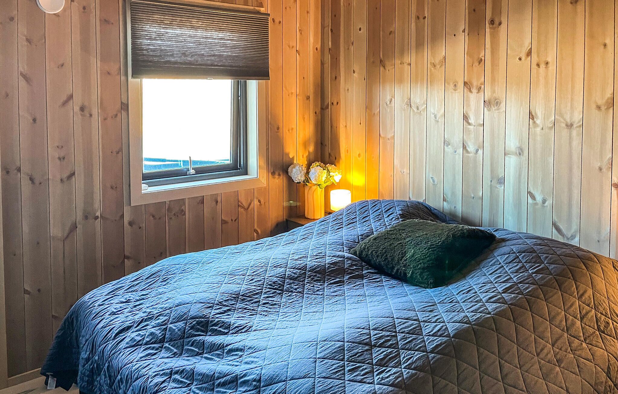 Een slaapkamer met een bed, een raam en een nachtkastje met een lamp.