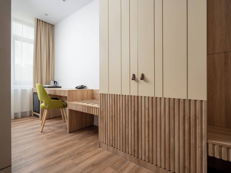 Una habitación moderna con un escritorio de madera, una silla verde y un armario amplio con listones verticales.
