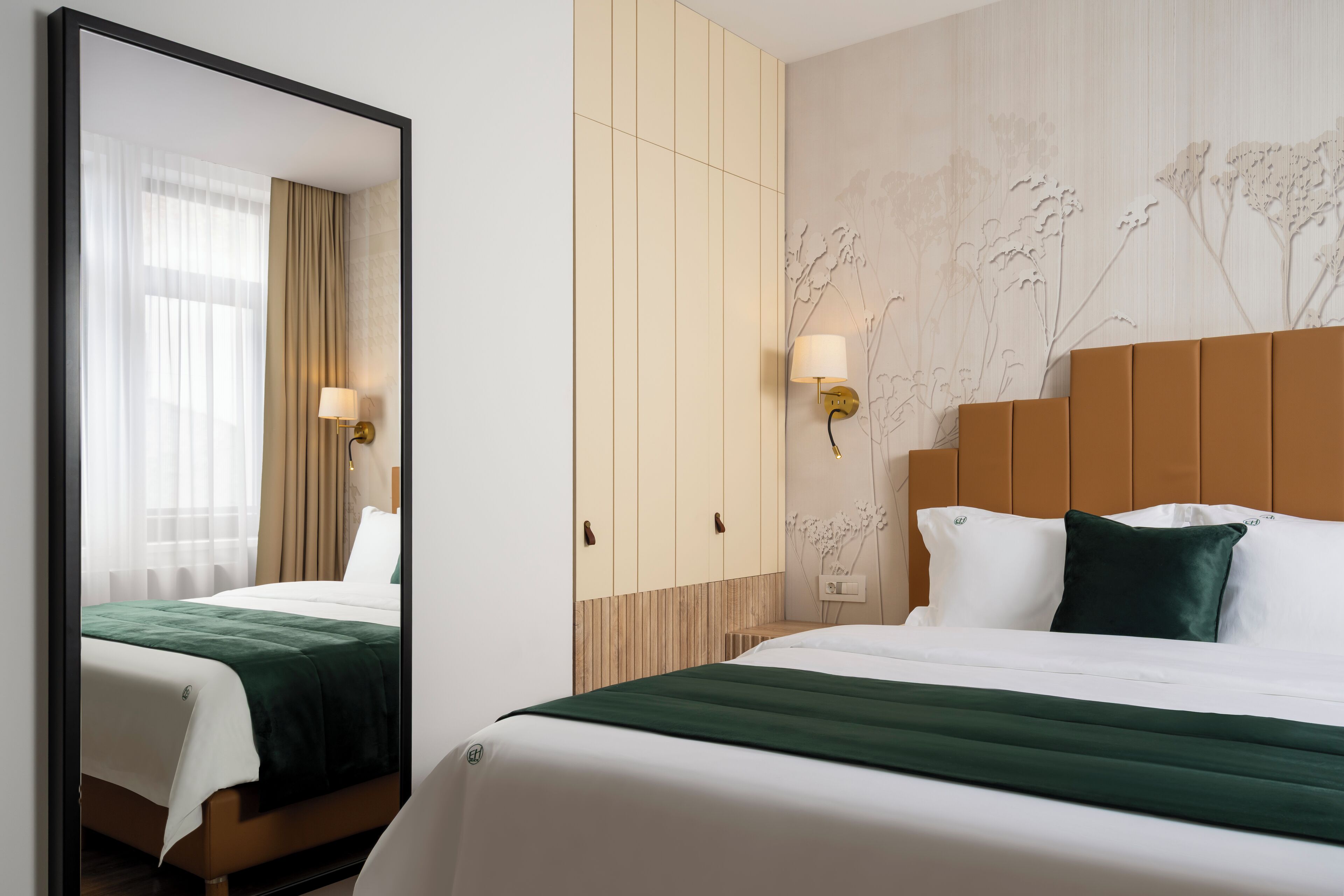 Habitación de hotel con cama, espejo, armario y pared con papel tapiz floral.