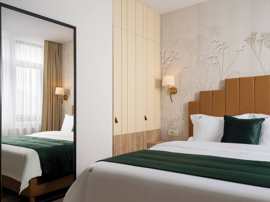 Habitación de hotel con cama, espejo, armario y pared con papel tapiz floral.