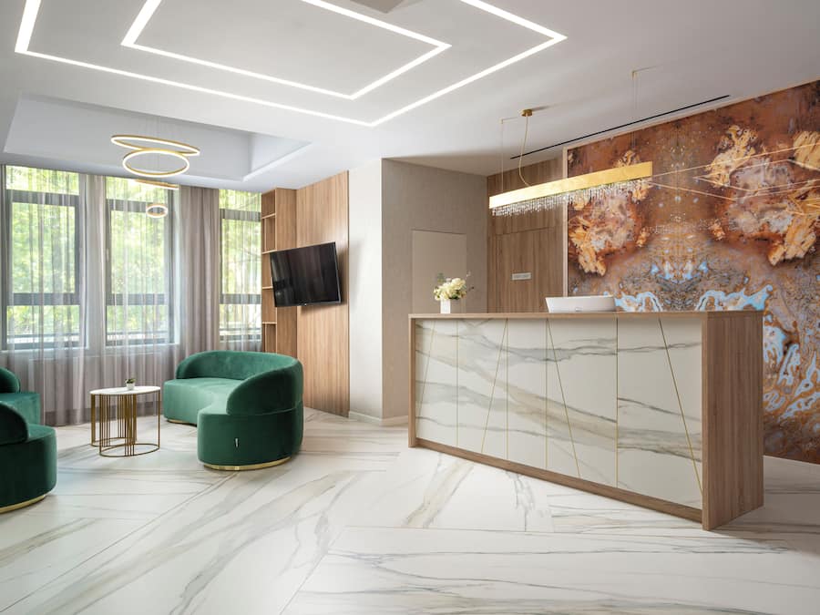 A modern hotel lobby with a marble floor, green upholstered seating, a wooden reception desk, and a large abstract mural on the wall.