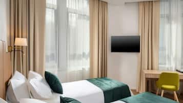 A hotel room with two beds, a desk, a chair, and a TV on the wall.