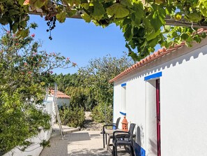 A covered outdoor area with a white building, a red door, and a table with chairs.