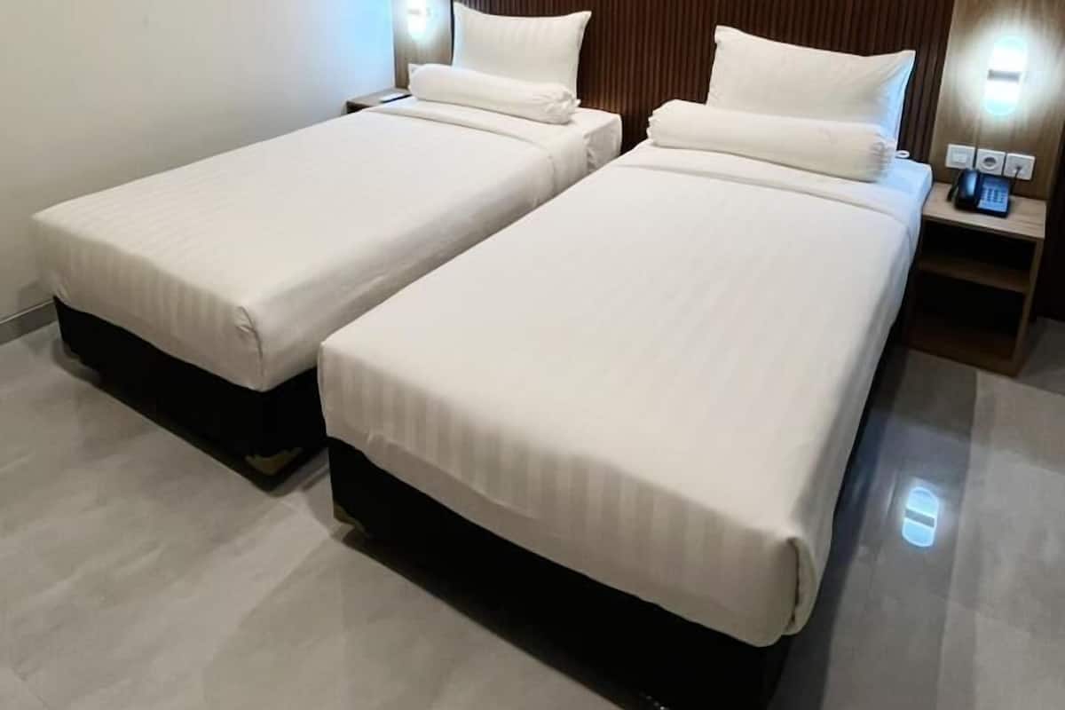 Une chambre d’hôtel avec deux lits, une tête de lit en bois, des lampes de chevet et une petite table avec un téléphone.
