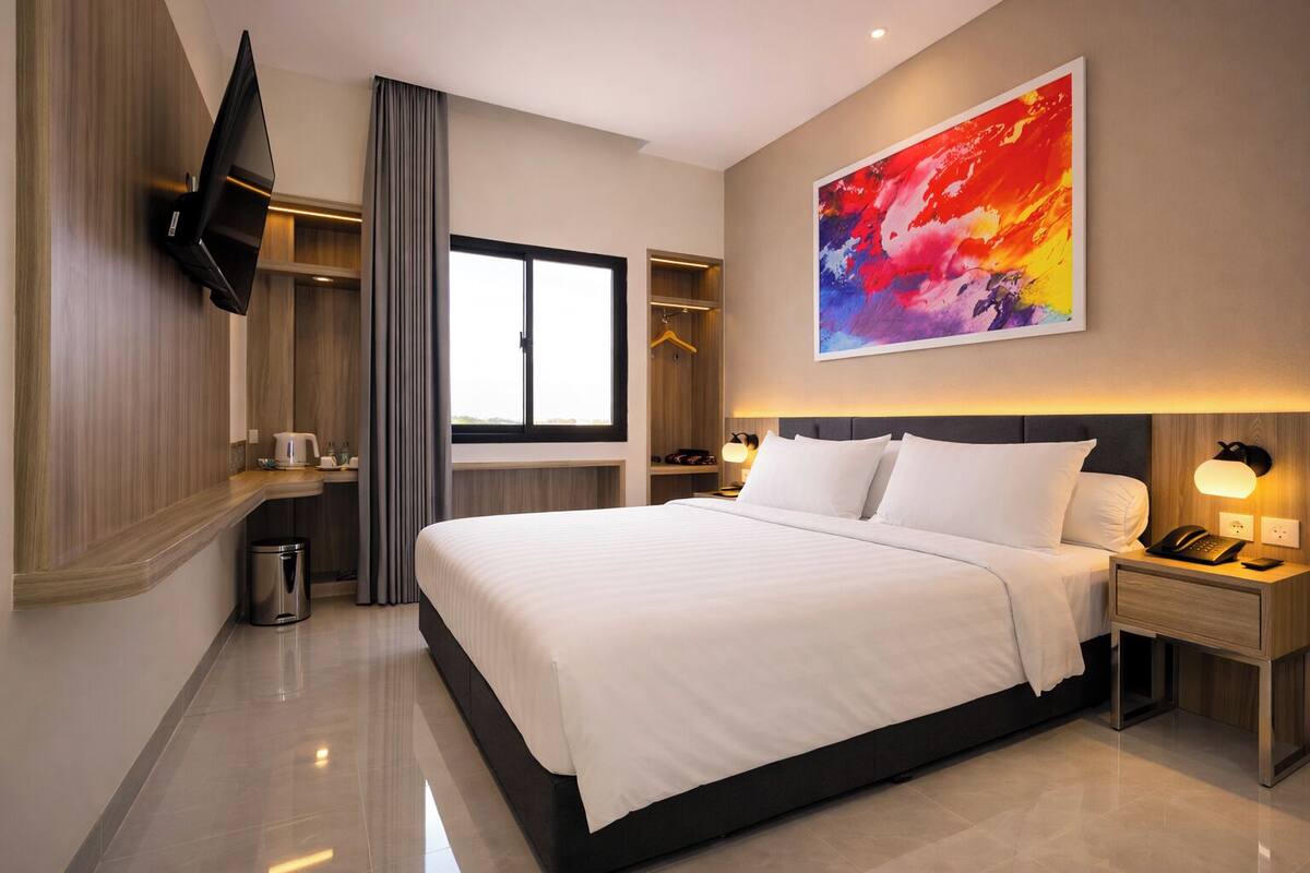 Une chambre d’hôtel moderne dotée d’un grand lit, d’un téléviseur à écran plat fixé au mur, d’une table de chevet avec une lampe et d’une fenêtre avec des rideaux.