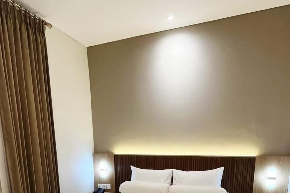 Une chambre d’hôtel avec un grand lit, deux tables de chevet avec des lampes, une tête de lit et un rideau.