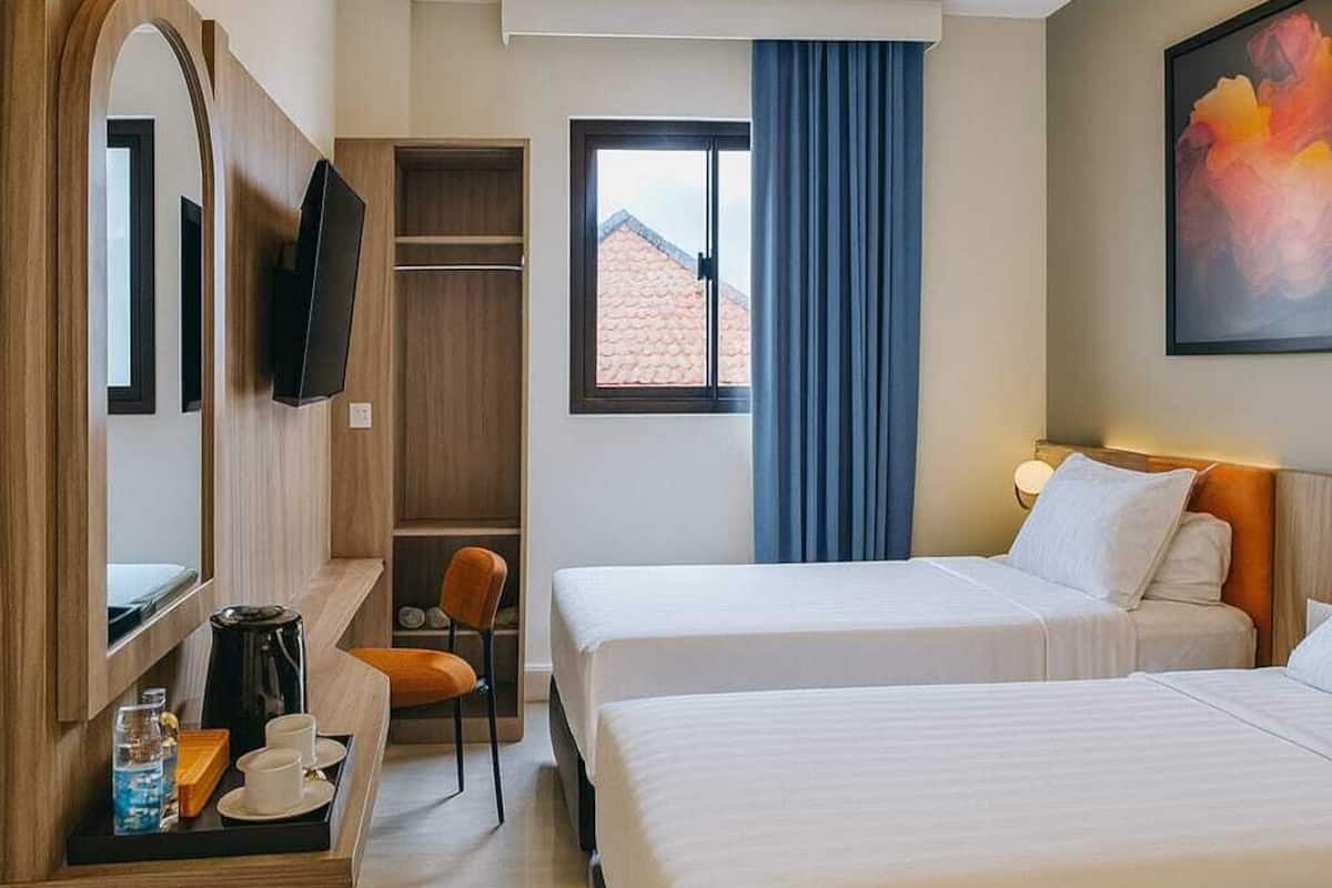 Une chambre d’hôtel avec deux lits, une télévision, un bureau avec une chaise et une fenêtre avec des rideaux.