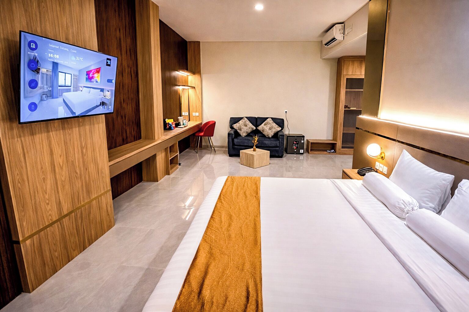 Een moderne hotelkamer met een groot bed, een bureau, een stoel, een bank en een aan de muur bevestigde televisie.