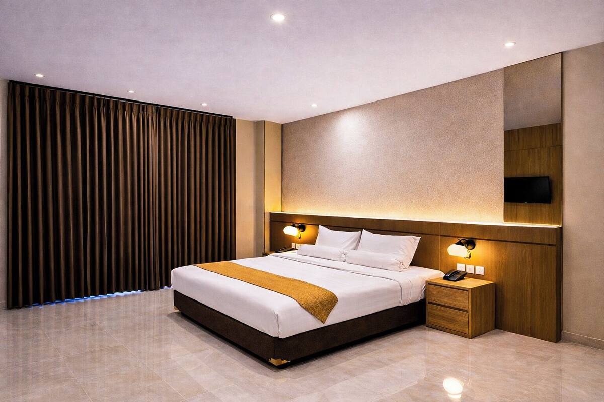 Une chambre d’hôtel moderne avec un grand lit, une table de chevet, un téléviseur fixé au mur et une fenêtre recouverte de rideaux.