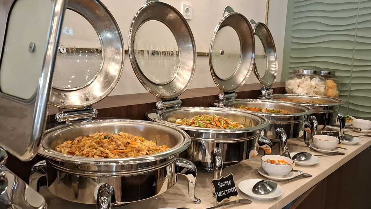 A buffet with multiple stainless steel chafing dishes, some labeled with food types like "Sausage Vegetables".