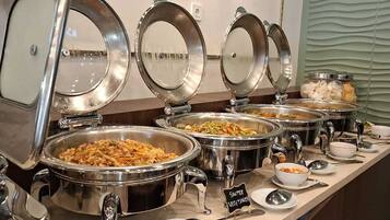 A buffet with multiple stainless steel chafing dishes, some labeled with food types like "Sausage Vegetables".