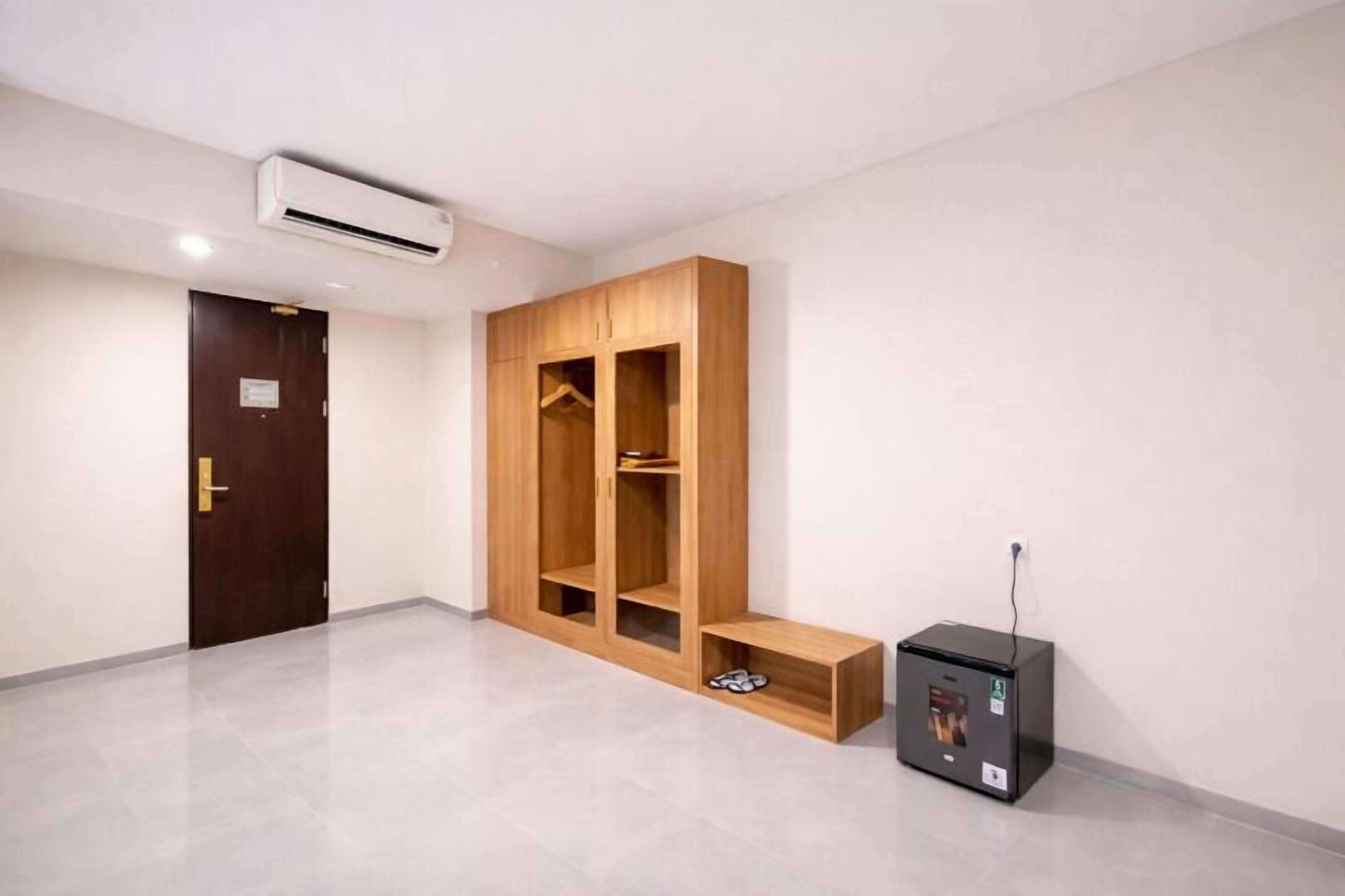 A room with a wooden wardrobe, a small bench, and a black electronic device on the floor.